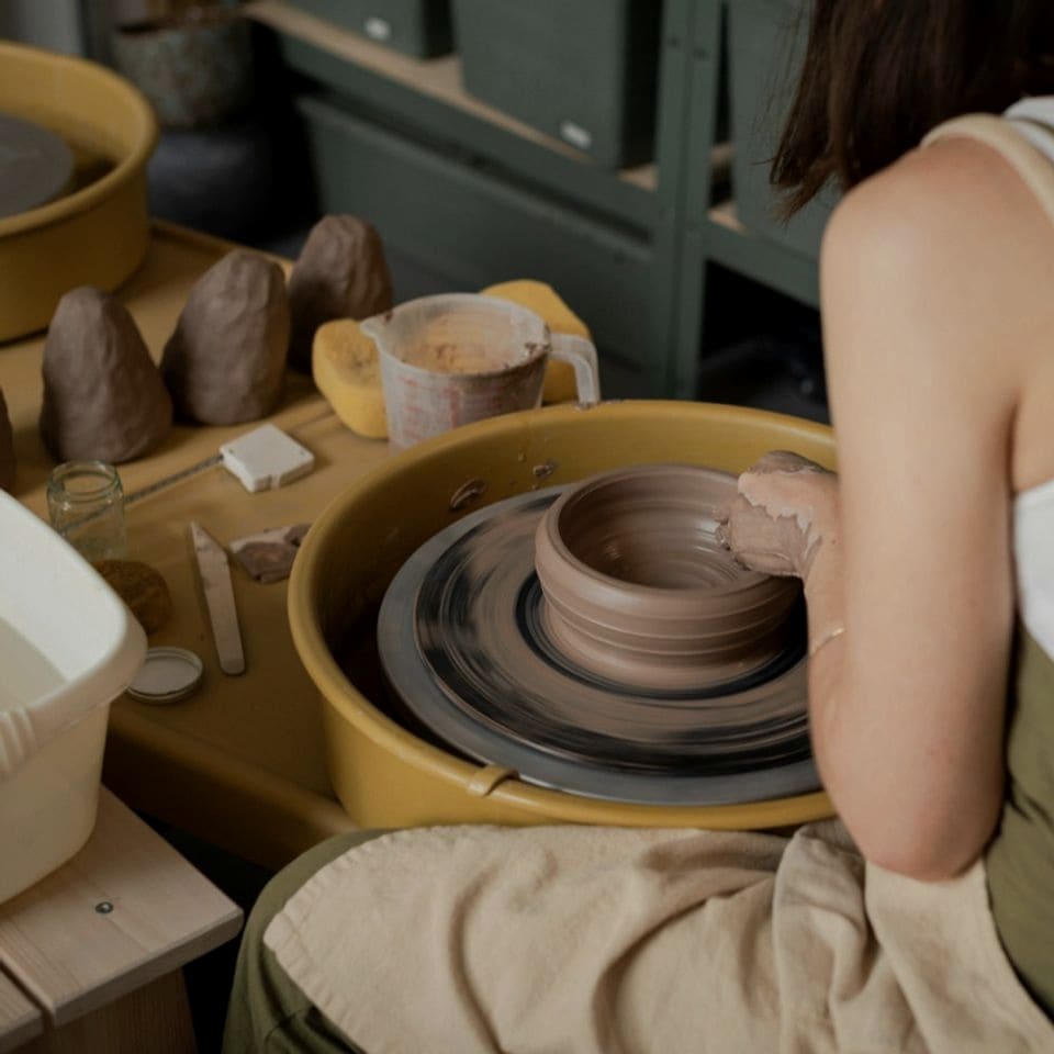 A ceramic artist shaping a clay vessel at the pottery wheel.